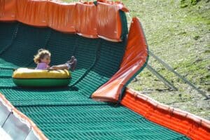 Kind rutscht lachend auf einem Tubing-Reifen eine Sommer-Tubing-Bahn hinunter – Familienhotel Petschnighof in Kärnten, aktives Freizeitangebot für Familien mit Kindern