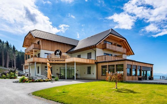 Das Familienhotel Petschnighof mit moderner Holzfassade, großen Balkonen und Bergblick bei blauem Himmel.